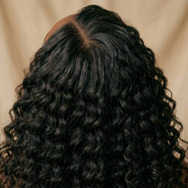 Close-up of a person with curly black hair against a beige background