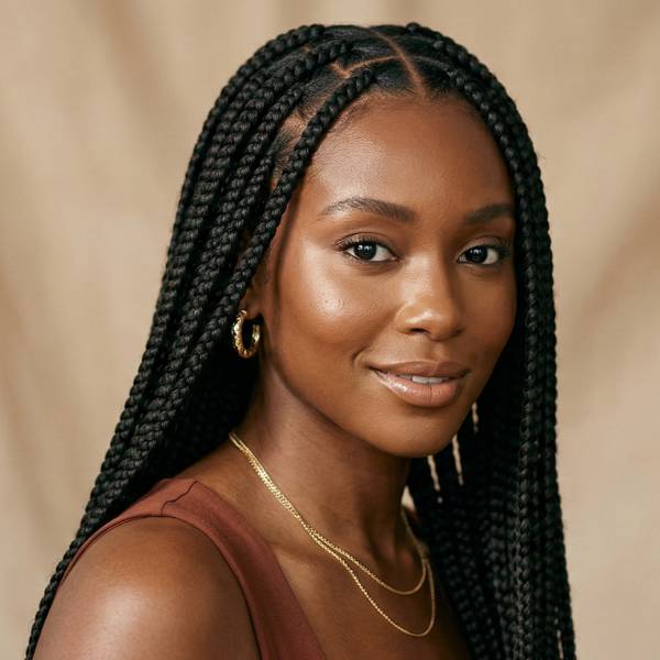 Woman with braided hair wearing gold jewelry against a beige background
