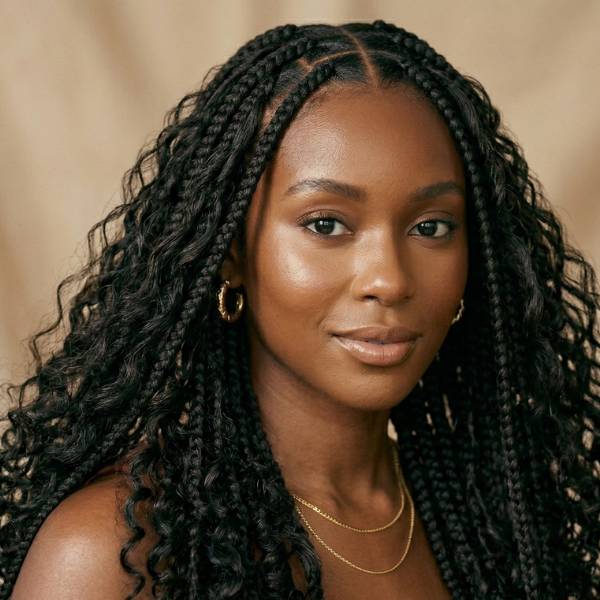 Woman with braided hair wearing gold earrings and a necklace against a beige background